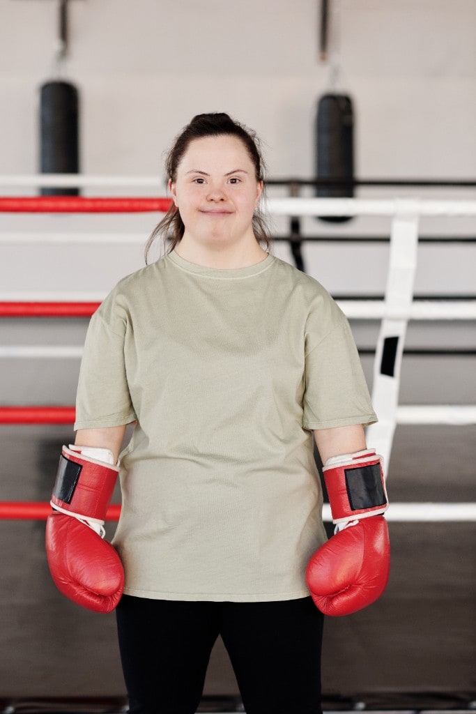 A smiling young woman with Down syndrome wearing red boxing gloves in a boxing gym