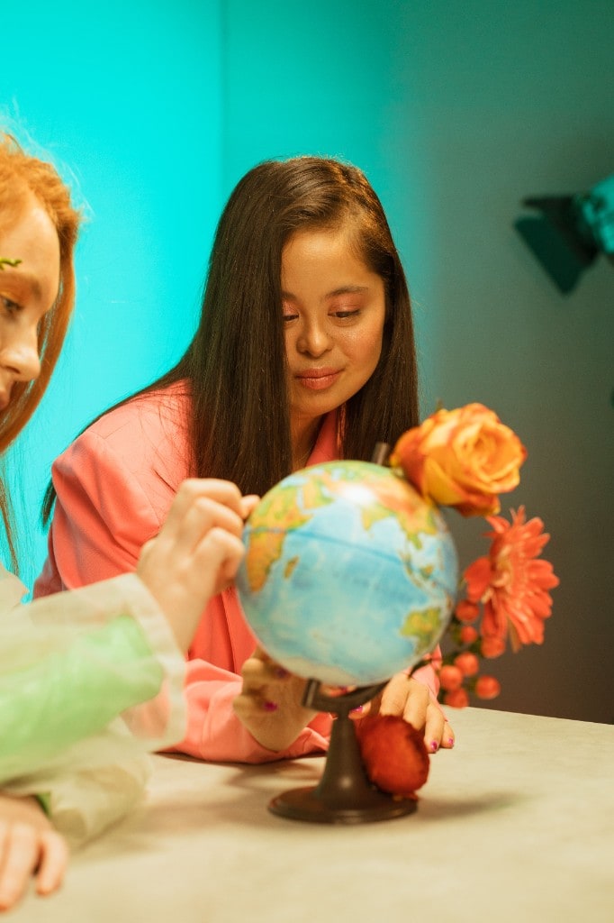 A young woman in a pink blazer looking at a small globe decorated with flowers
