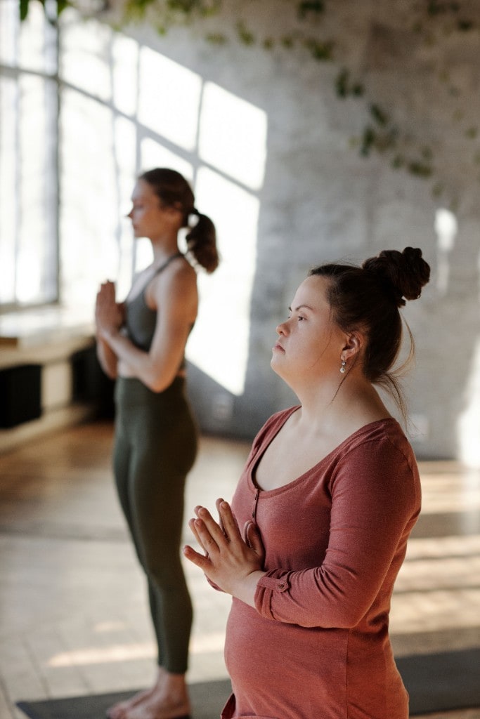 A young woman with Down syndrome practicing yoga in a prayer pose in a sunlit studio